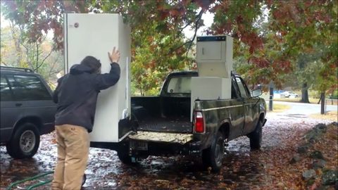 a man loads a white refrigerator onto a pickup truck bed by himself