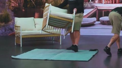 mover carrying a wicker patio armchair across a patio
